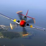 P-51 Mustang warbird met rode staart boven een kustlandschap